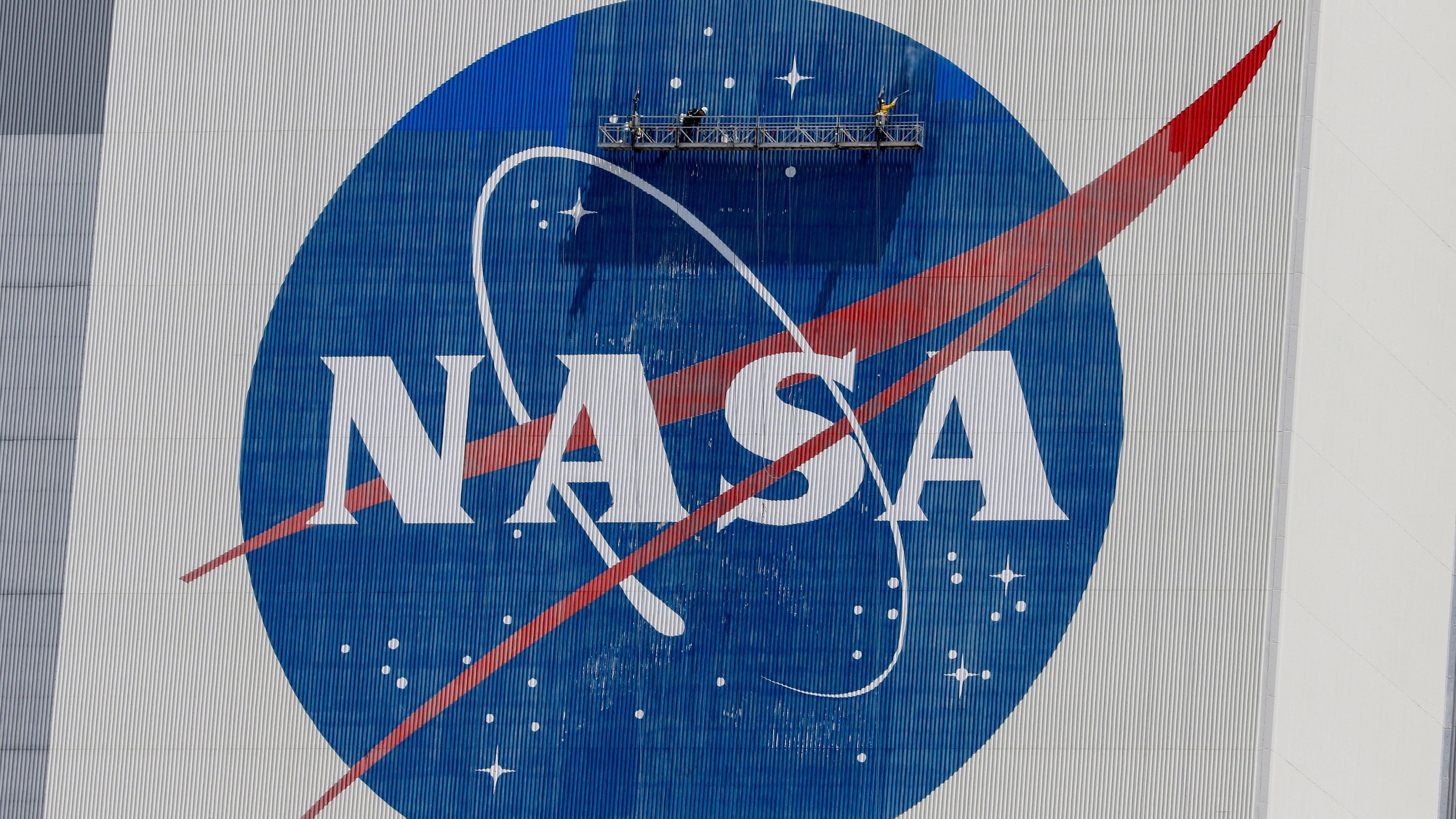 <div class="paragraphs"><p>Workers pressure wash the logo of NASA</p></div>