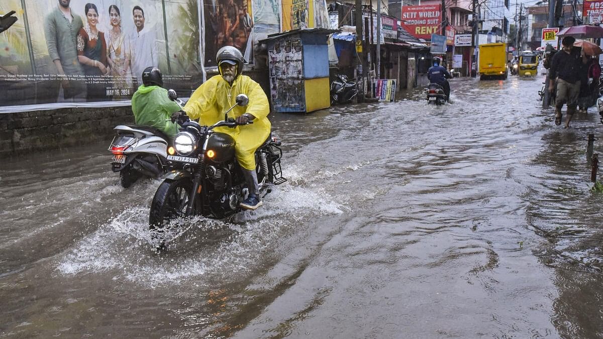 <div class="paragraphs"><p>Commuters wade through a flooded road amid rains, in Kochi.</p></div>