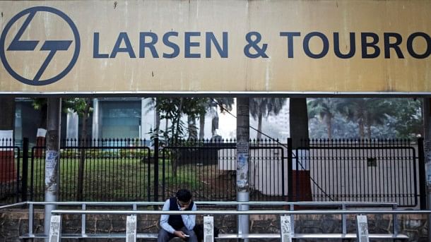 <div class="paragraphs"><p>A man sits below a Larsen &amp; Toubro board.</p></div>