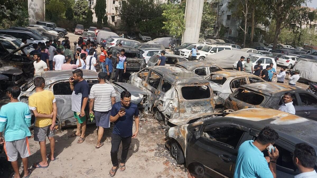 <div class="paragraphs"><p>Residents stand near charred vehicles a day after a fire broke out at a civic authority-run parking lot in Madhu Vihar area of east Delhi.</p></div>