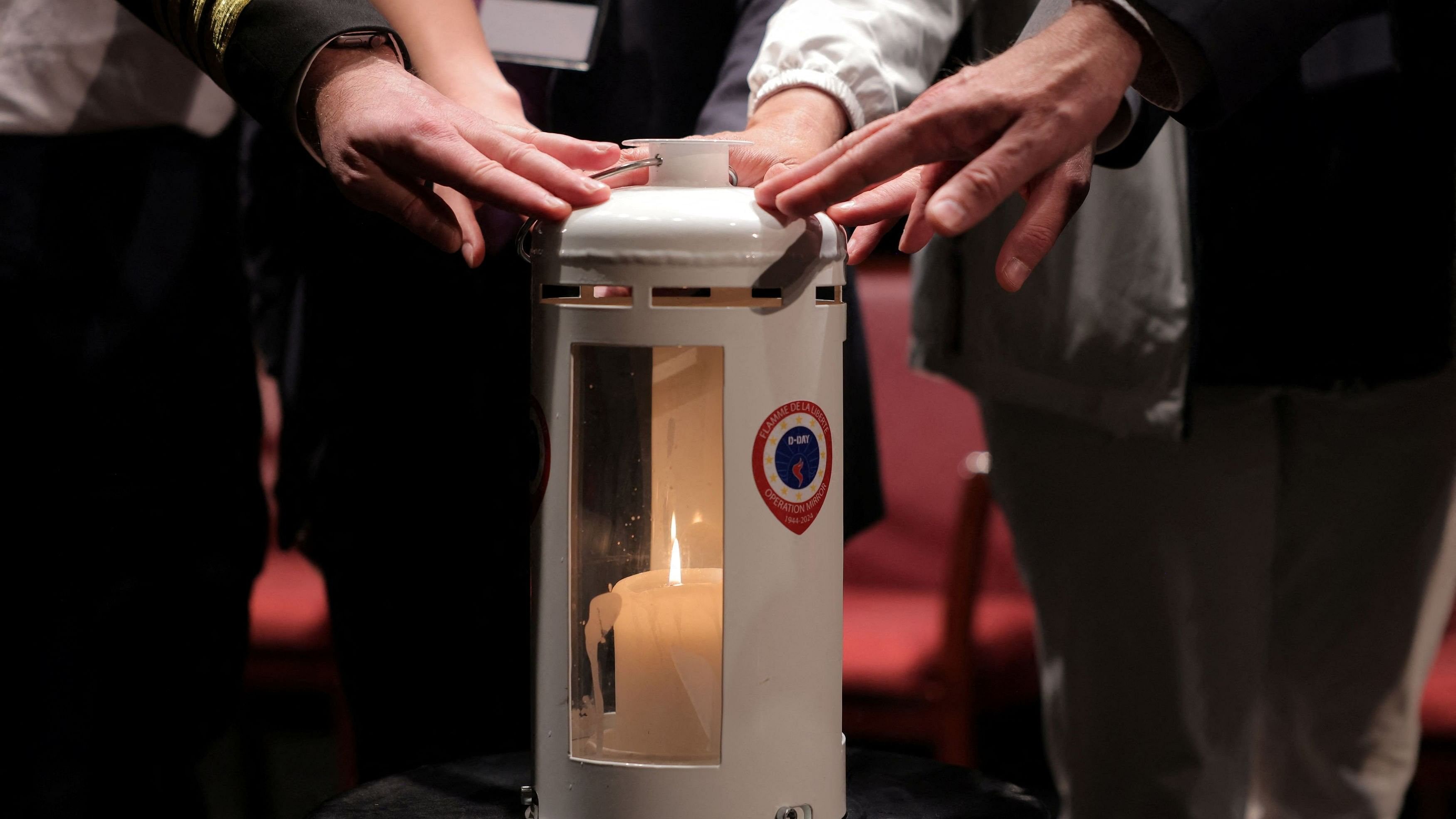 <div class="paragraphs"><p>Attendees place their hands on a candle containing France's Eternal Flame after it arrived from France on the Queen Mary 2 for a commemorative ceremony honoring the Normandy landings of 1944 and marking the upcoming 80th Anniversary of D-Day, in Brooklyn, New York City.&nbsp;</p></div>