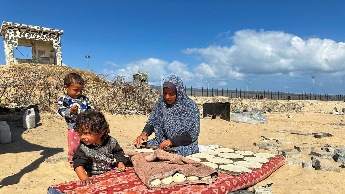 <div class="paragraphs"><p>A woman prepares food next to children, as displaced Palestinians take shelter at the border with Egypt, during an Israeli military operation, in Rafah in the southern Gaza Strip.</p></div>