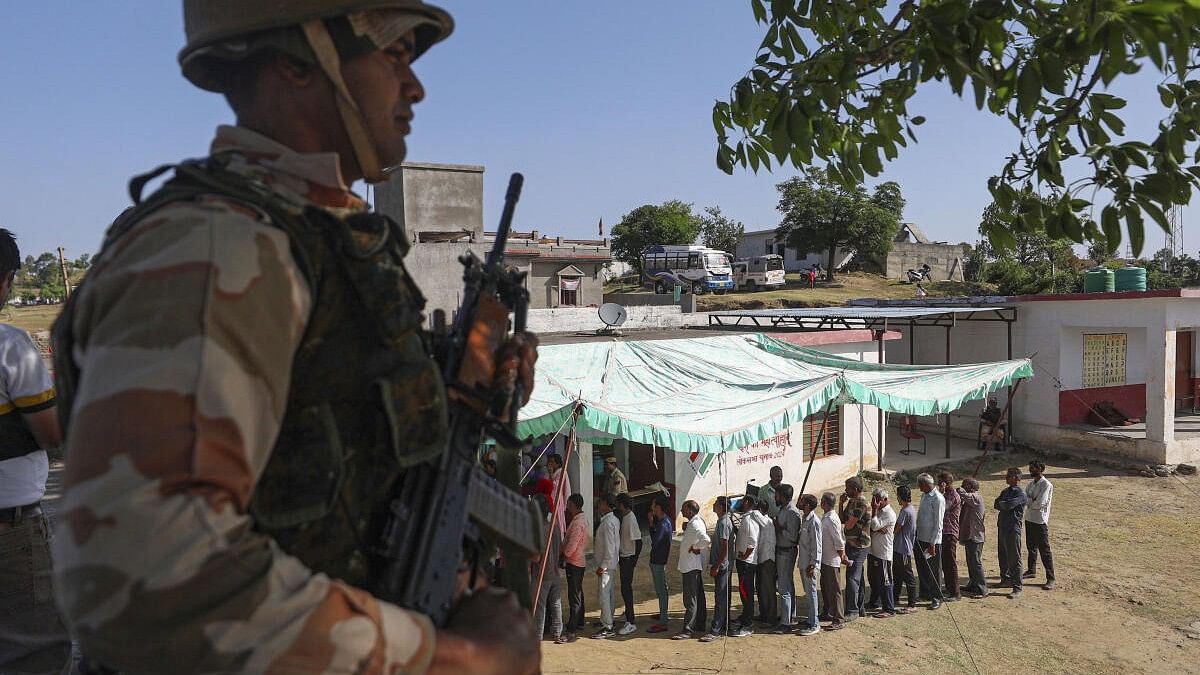 <div class="paragraphs"><p>A security personnel stands guard as people wait in a queue to cast their votes at a polling booth during the sixth phase of Lok Sabha elections, at Nowshera, in Rajouri district.</p></div>