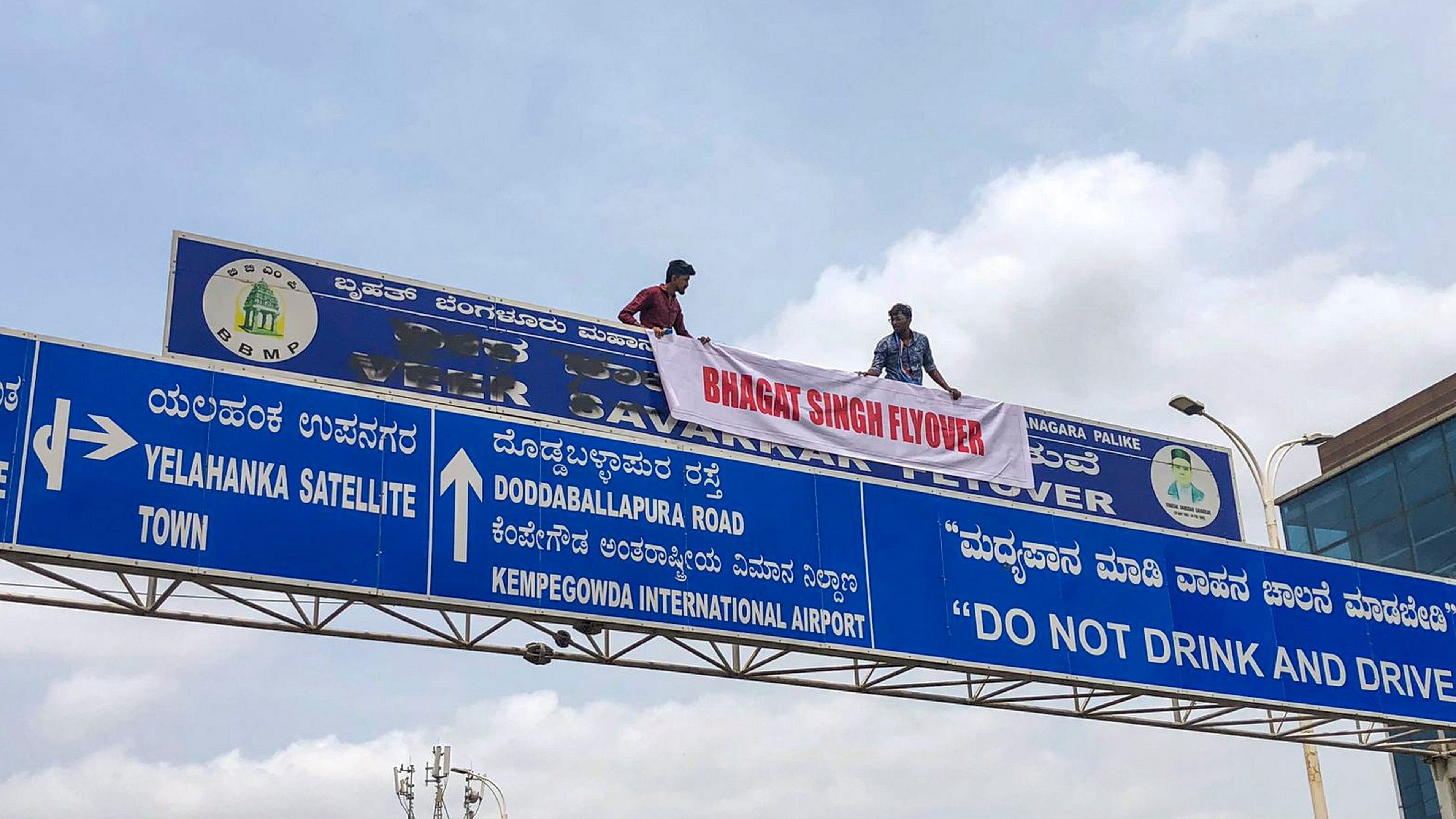 <div class="paragraphs"><p> NSUI members hang a banner that reads 'Bhagat Singh Flyover' over a signboard of Veer Savarkar Flyover, in Bengaluru, Tuesday.</p></div>