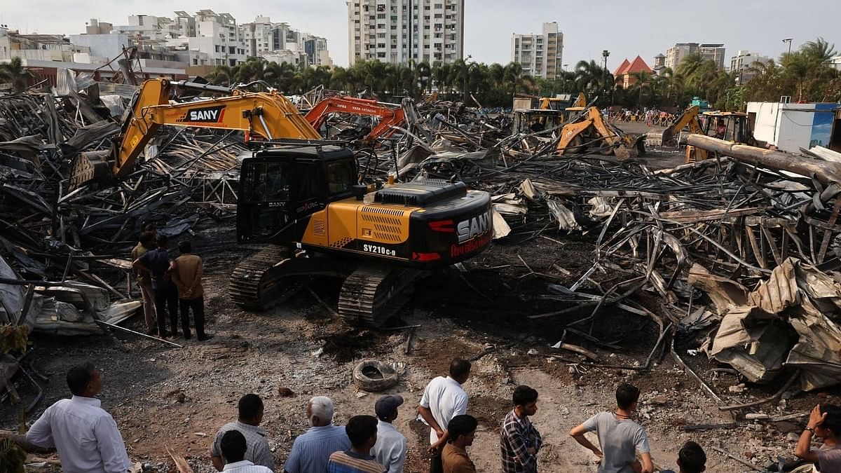 <div class="paragraphs"><p>Machines move debris as onlookers watch following a fire in a gaming zone in Rajkot.</p></div>