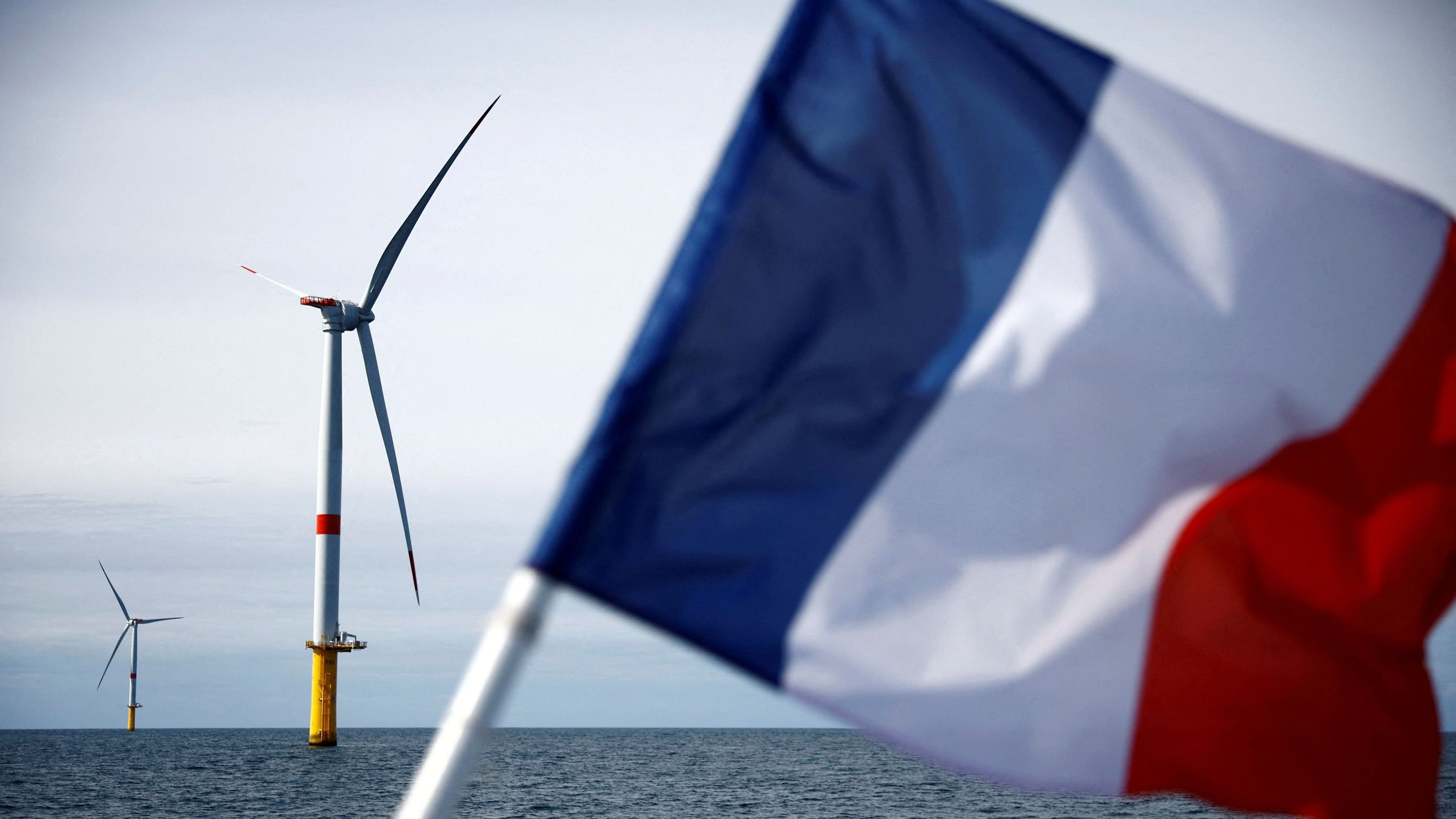 <div class="paragraphs"><p>A French flag flies in front of wind turbines at the Saint-Nazaire offshore wind farm, off the coast of the Guerande peninsula in western France.&nbsp;</p></div>