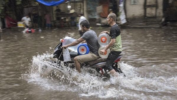 <div class="paragraphs"><p>Commuters wade through a waterlogged street following rains, in Surat, Sunday.&nbsp;</p></div>