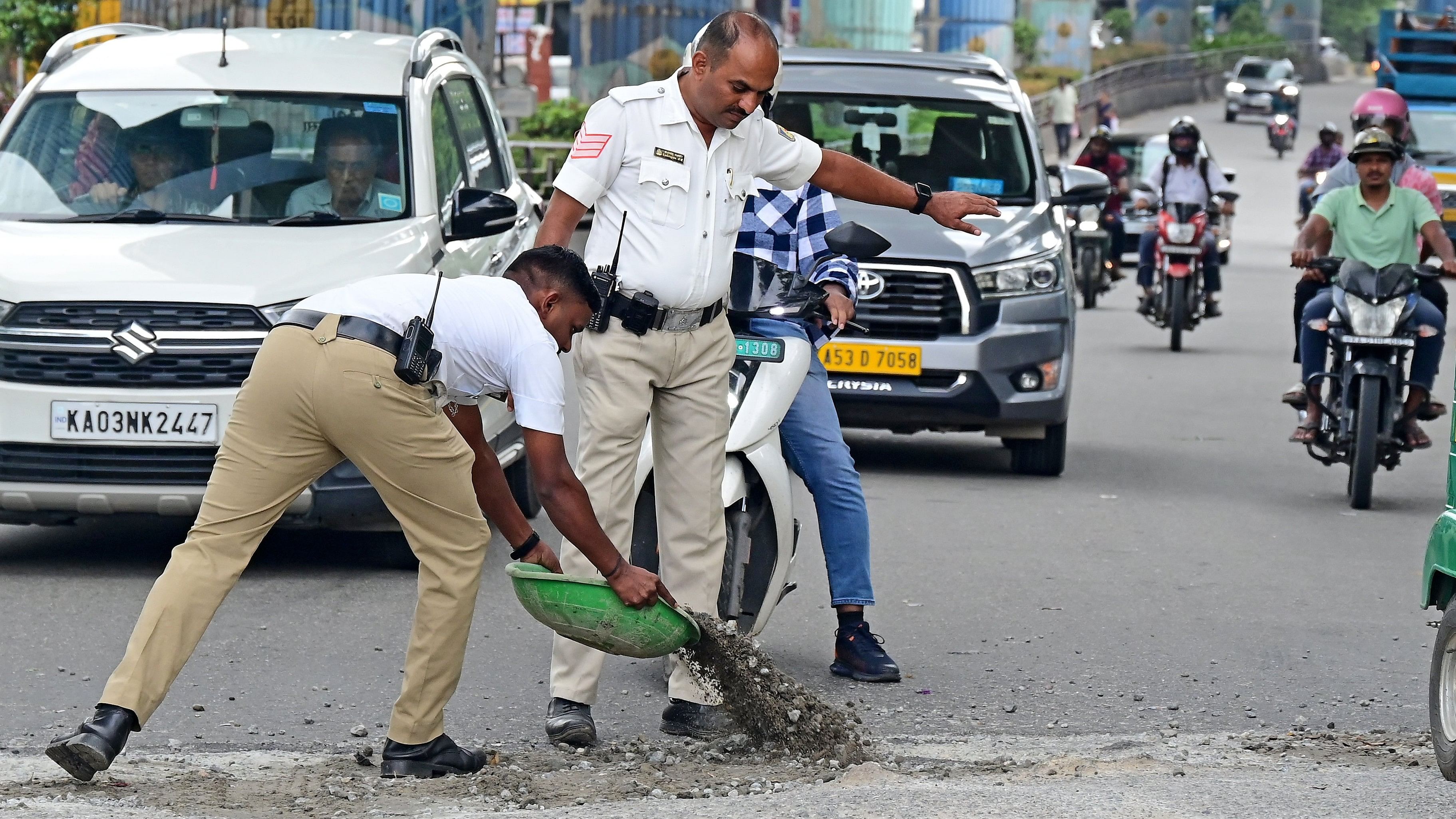 <div class="paragraphs"><p>Traffic policemen fill a pothole at Kimco Junction in Deepanjali Nagar, Mysuru Road. Potholes turn into ponds after a heavy&nbsp;downpour, affecting vehicular movement. </p></div>