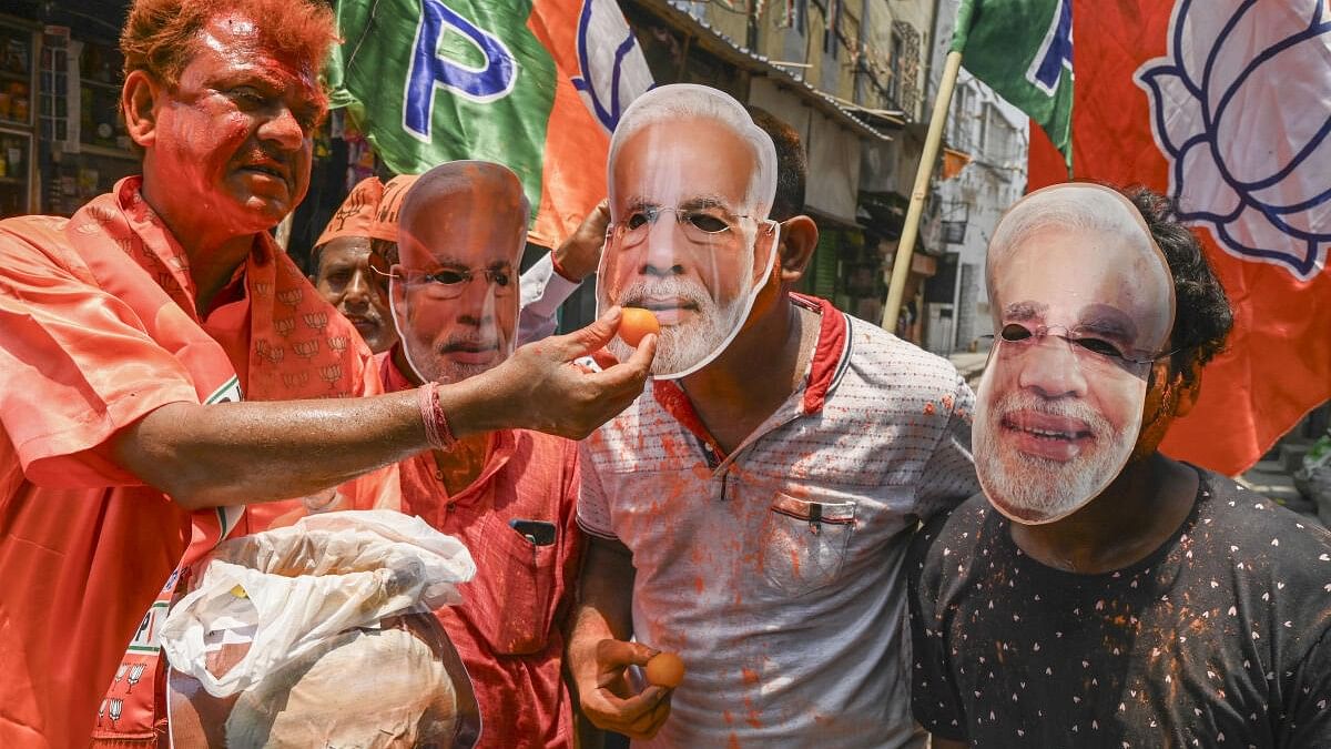 <div class="paragraphs"><p>Supporters of Prime Minister-designate Narendra Modi’s mask, offer sweets to one another ahead of Modi’s swearing-in ceremony as prime minister for the third consecutive term.</p></div>