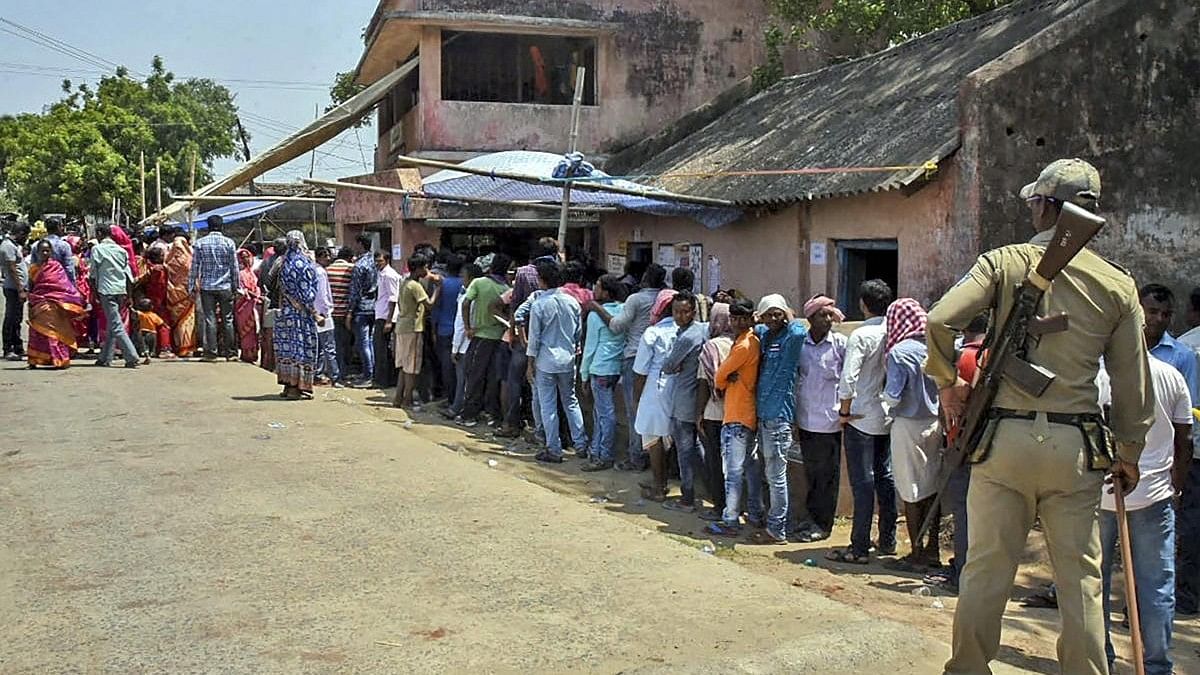 <div class="paragraphs"><p>A security personnel stands guard as voters queue outside a polling station to cast their vote.</p></div>