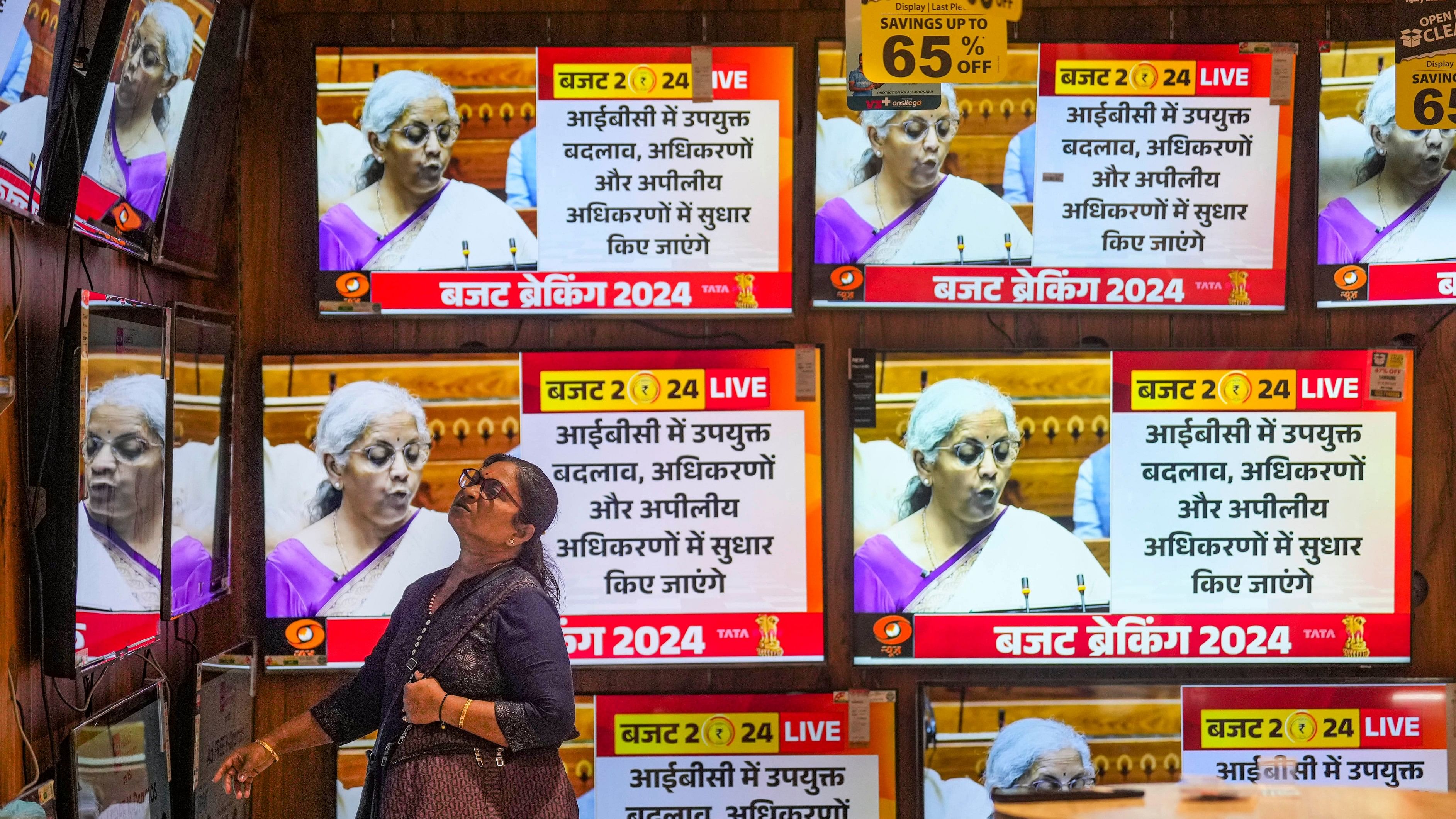 <div class="paragraphs"><p>A woman watches the Union Budget 2024-25 being presented by Union Finance Minister Nirmala Sitharaman in the Lok Sabha on television screens, at a showroom in Mumbai.</p></div>