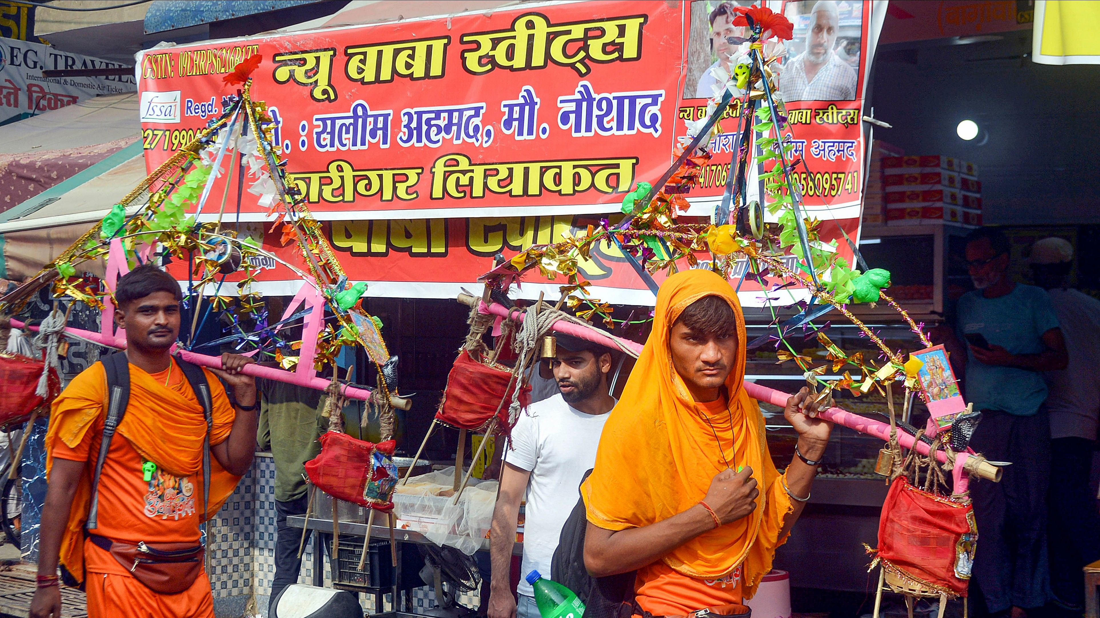 <div class="paragraphs"><p>Kanwariyas walk past a shop on which banners with shopkeeper's name was put up on Kanwar Marg after an order issued by Uttar Pradesh Government, in Muzaffarnagar.</p></div>