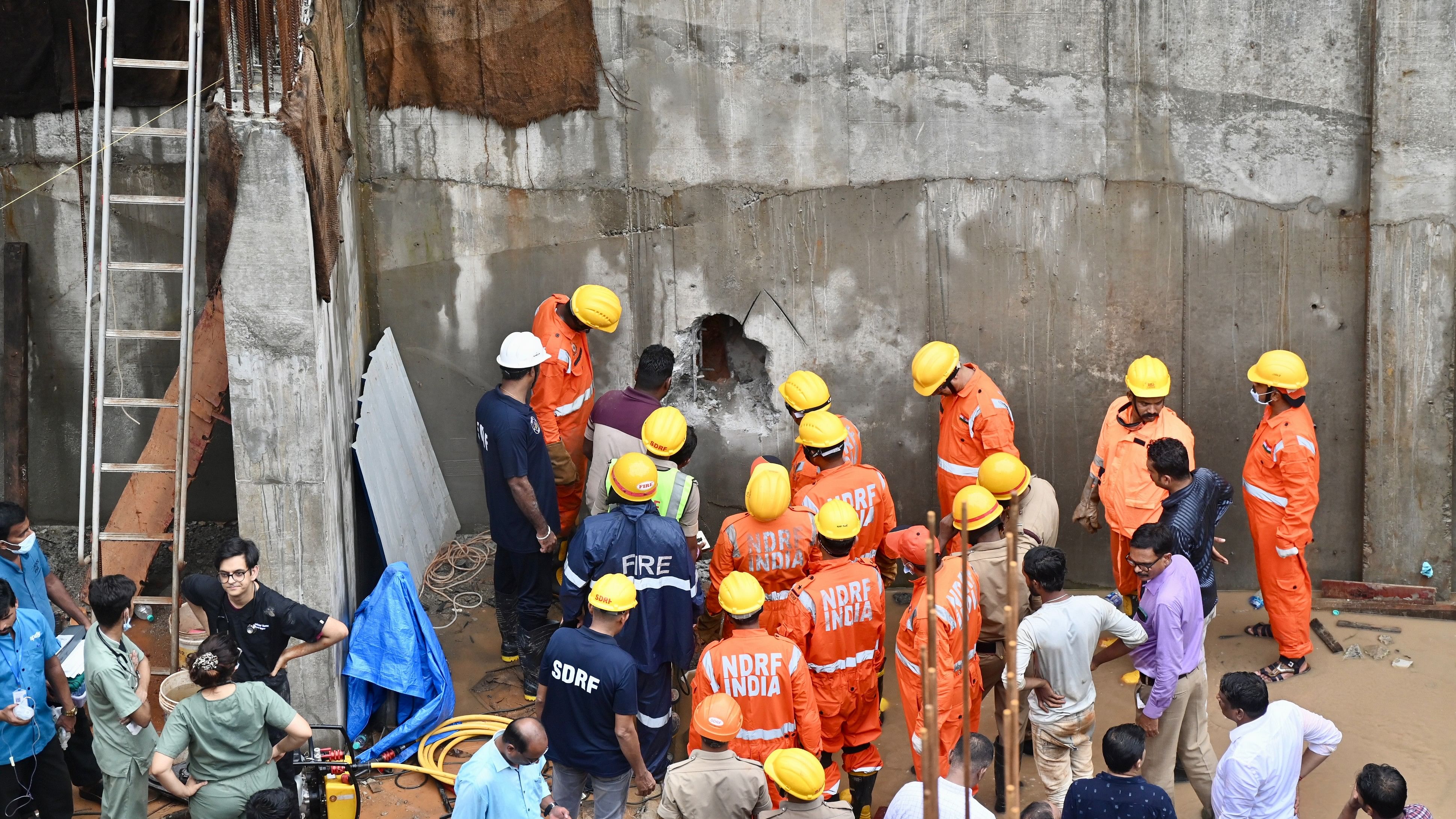 <div class="paragraphs"><p>Rescue teams seen drilling a hole through the concrete retaining wall in order to rescue a labouer trapped under the mounds of soil at a construction site in Balmatta in Mangaluru on Wednesday.</p></div>