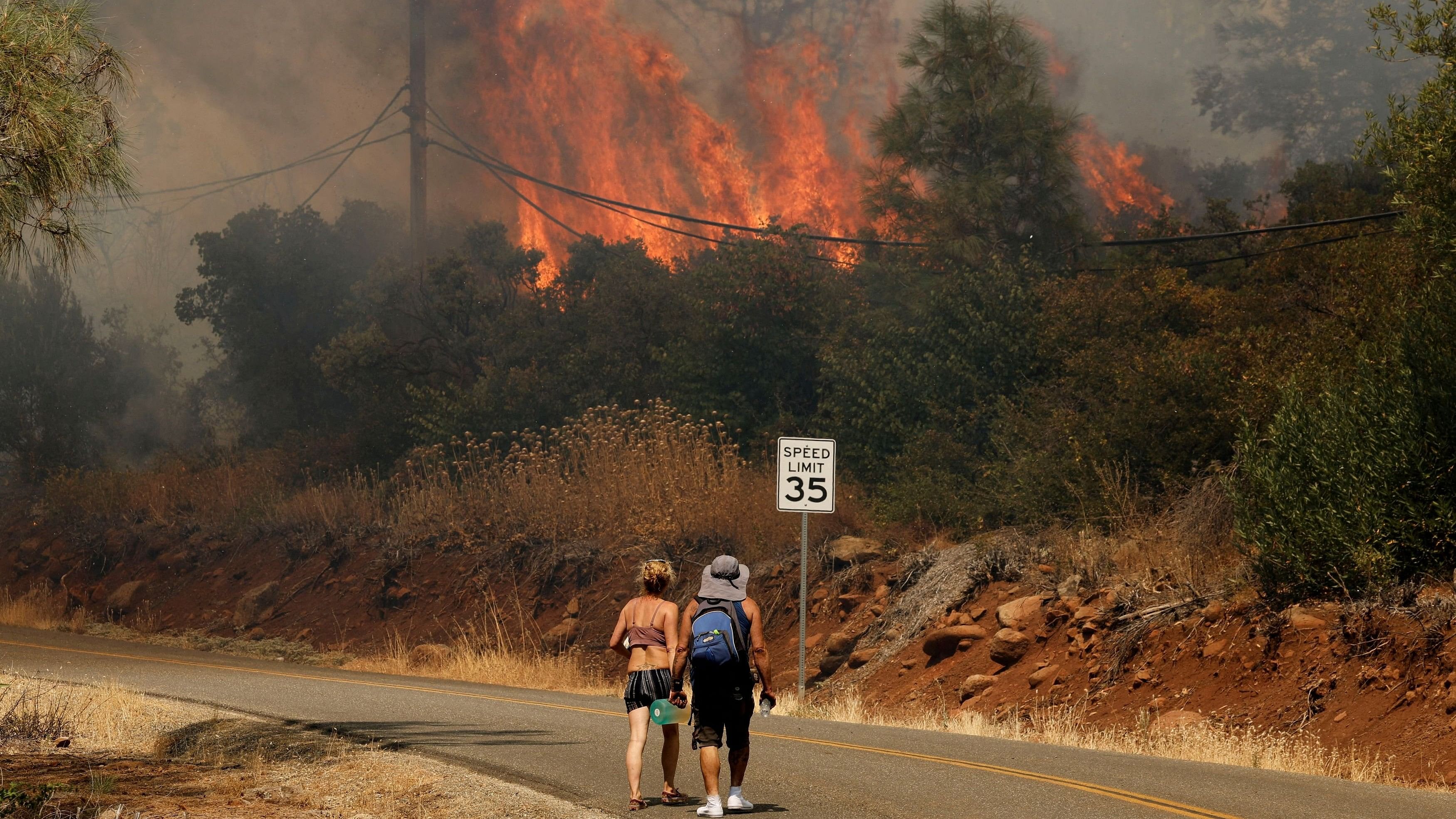 <div class="paragraphs"><p>People walk on the road near flames and smoke plume rising as firefighters continue to tackle the Park Fire in California.</p></div>