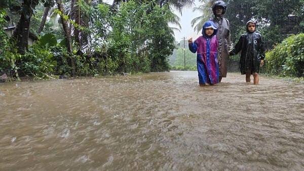 <div class="paragraphs"><p>A man along with children walks through a waterlogged street during rains, in Udupi district of Karnataka.</p></div>