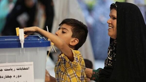 <div class="paragraphs"><p>An Iranian boy casts a vote next to a woman at a polling station in a snap presidential election to choose a successor to Ebrahim Raisi following his death in a helicopter crash, in Tehran, Iran June 28.</p></div>