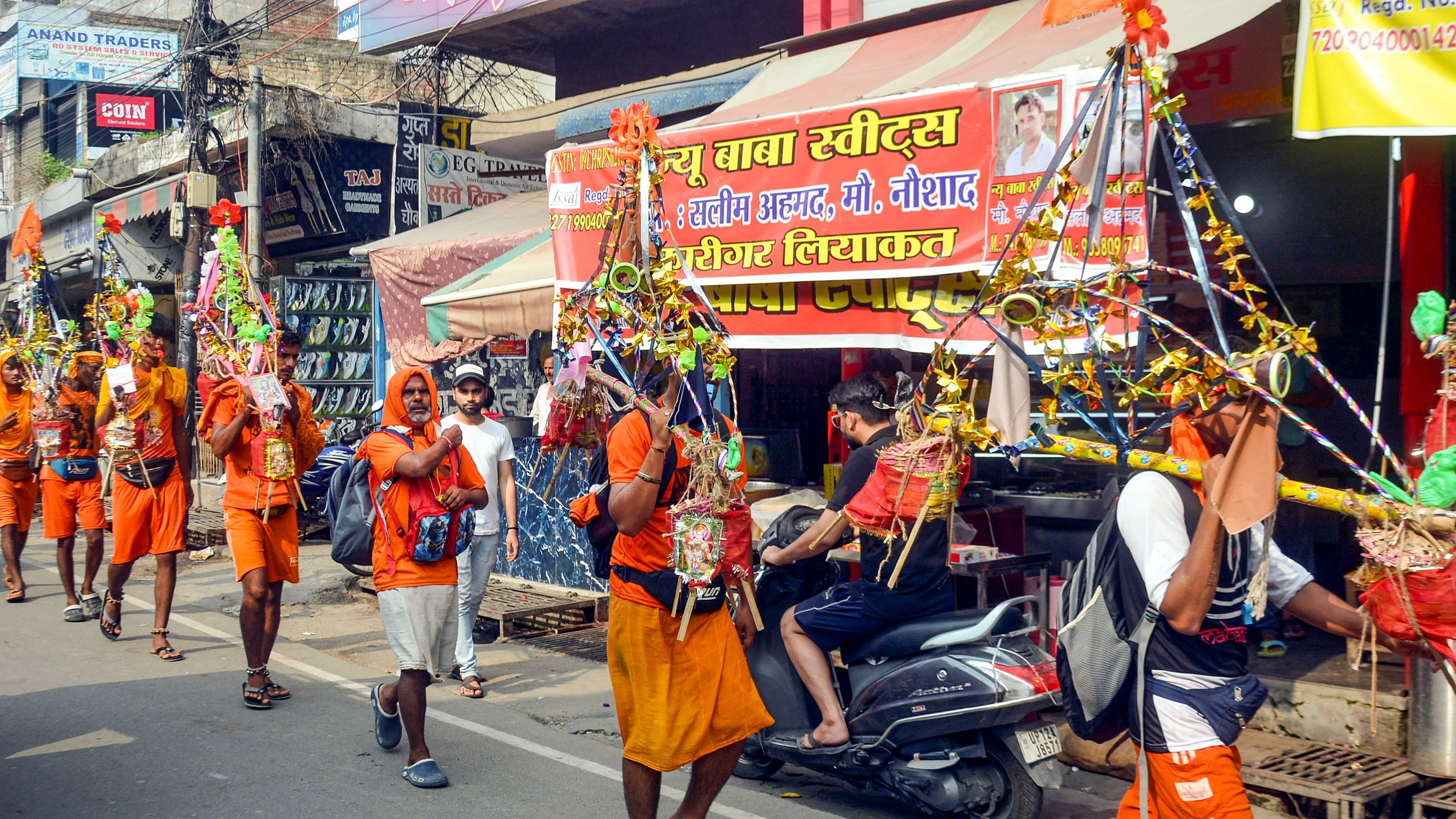 <div class="paragraphs"><p>Kanwariyas walk past the shops on which banners with shopkeepers' name were put up on Kanwar Marg after an order issued by Uttar Pradesh Government, in Muzaffarnagar, Saturday, July 20, 2024.</p></div>