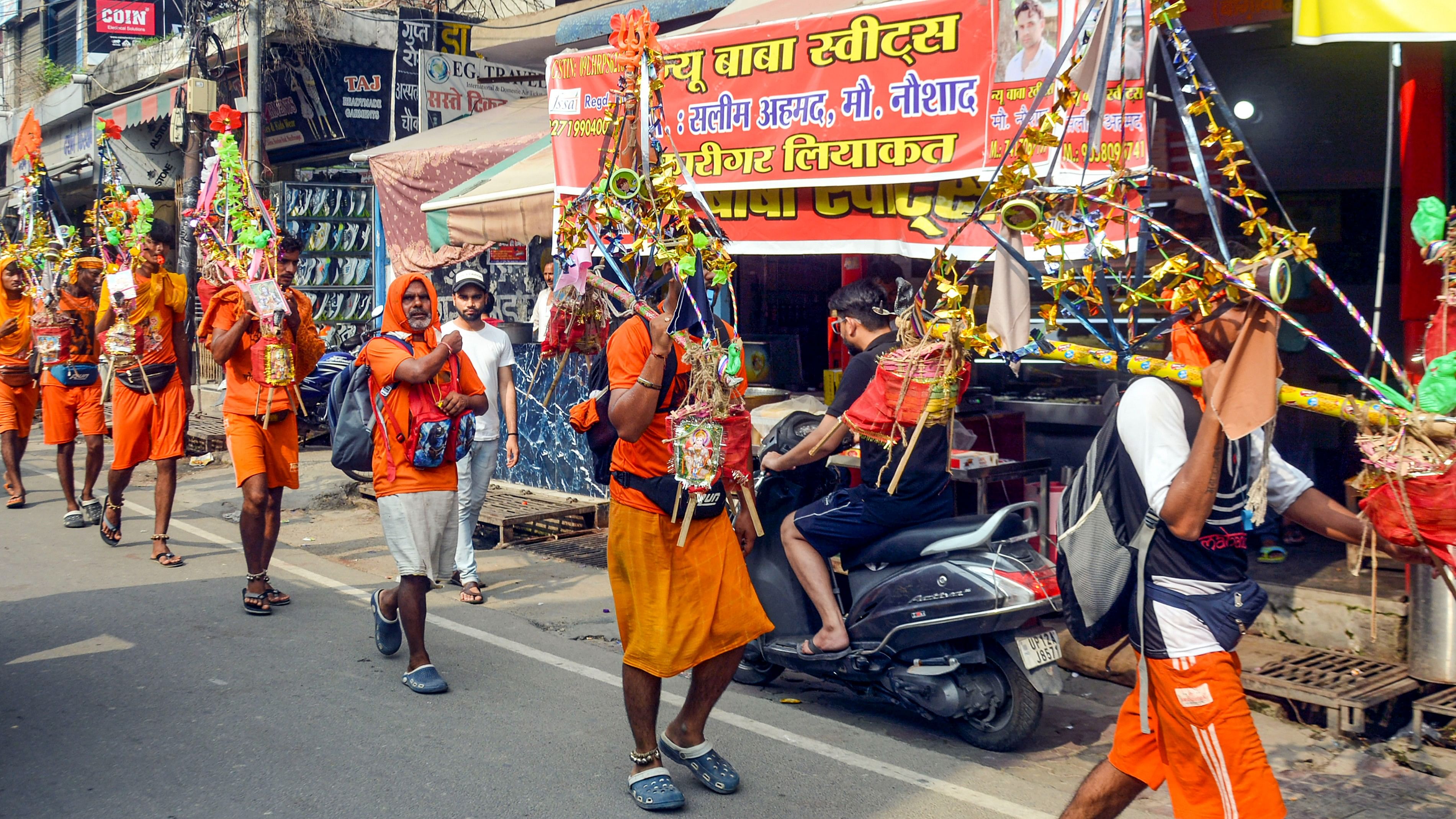 <div class="paragraphs"><p>Kanwariyas walk past the shops on which banners with shopkeepers' name were put up on Kanwar Marg after an order issued by Uttar Pradesh Government, in Muzaffarnagar, Saturday, July 20, 2024.</p></div>