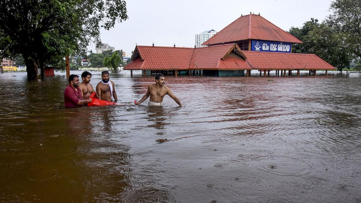 <div class="paragraphs"><p>People make their way through a flooded area near the Aluva Mahadeva Temple which got partially submerged due to rising water levels of the Periyar river following heavy rains, in Kochi.</p></div>