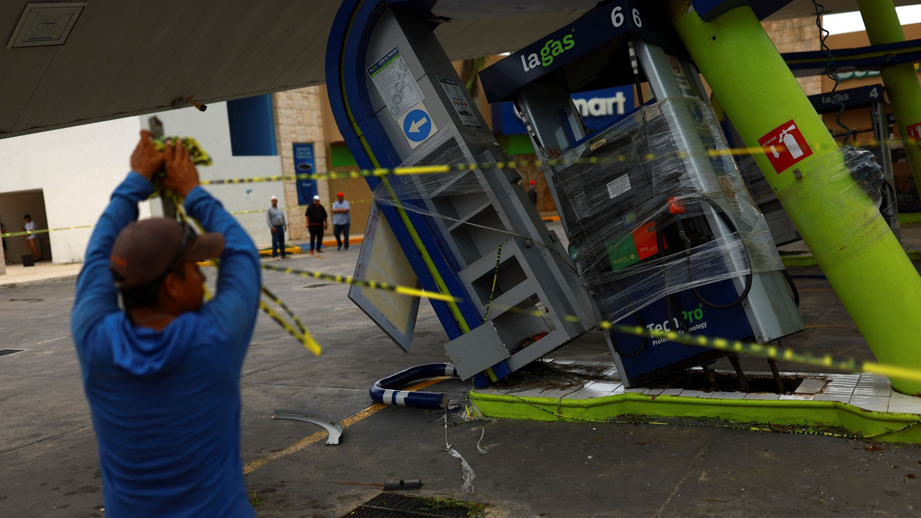 <div class="paragraphs"><p>A person holds caution tape around a gas station that was hit by Hurricane Beryl, which has now downgraded to tropical storm, in Puerto Aventuras, Mexico, July 5, 2024. </p></div>