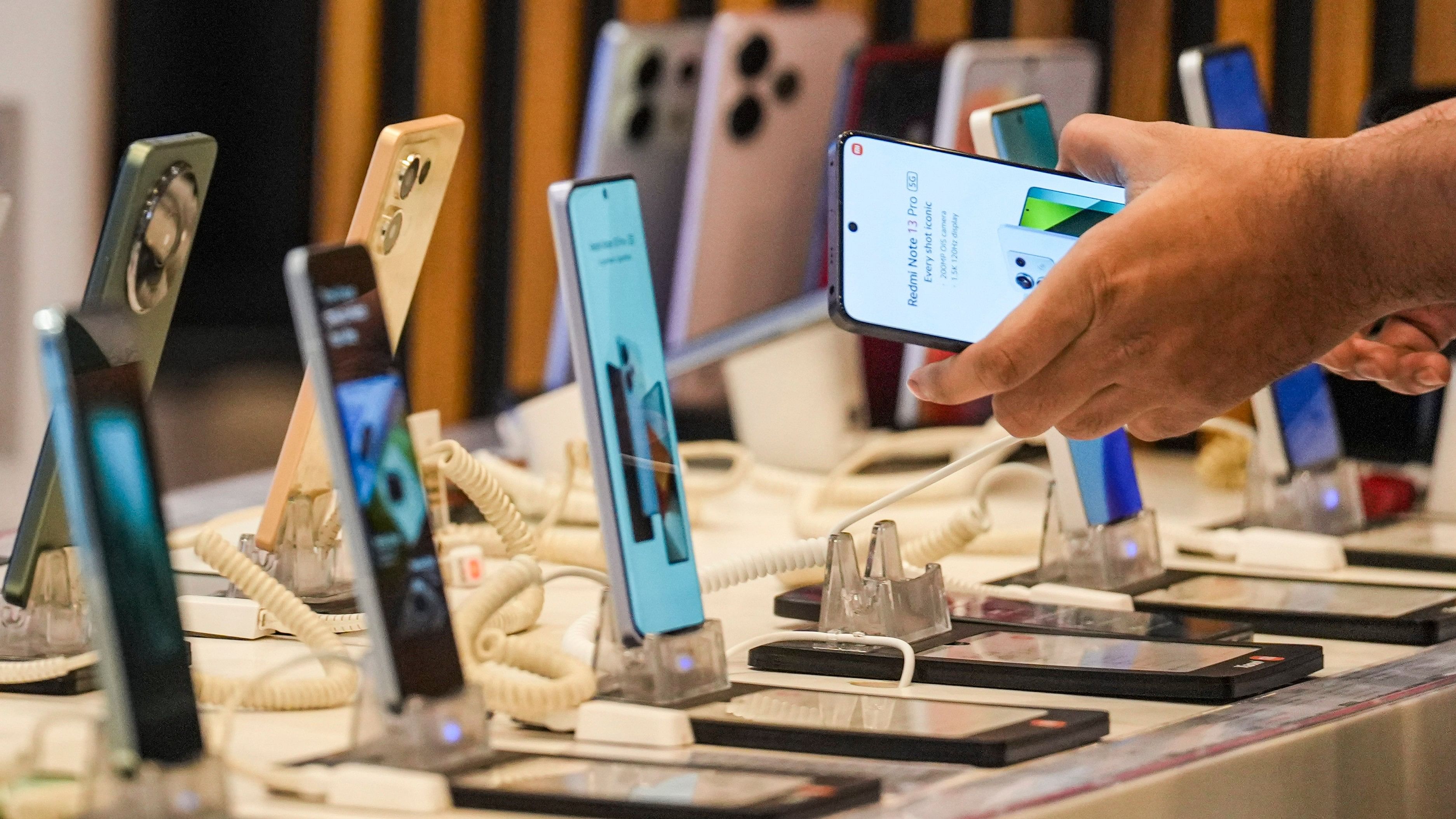 <div class="paragraphs"><p>A man checks mobile phones as Union Budget 2024-25 being presented by Union Finance Minister Nirmala Sitharaman in Lok Sabha, at a TV showroom in Mumbai, Tuesday, July 23, 2024. </p></div>