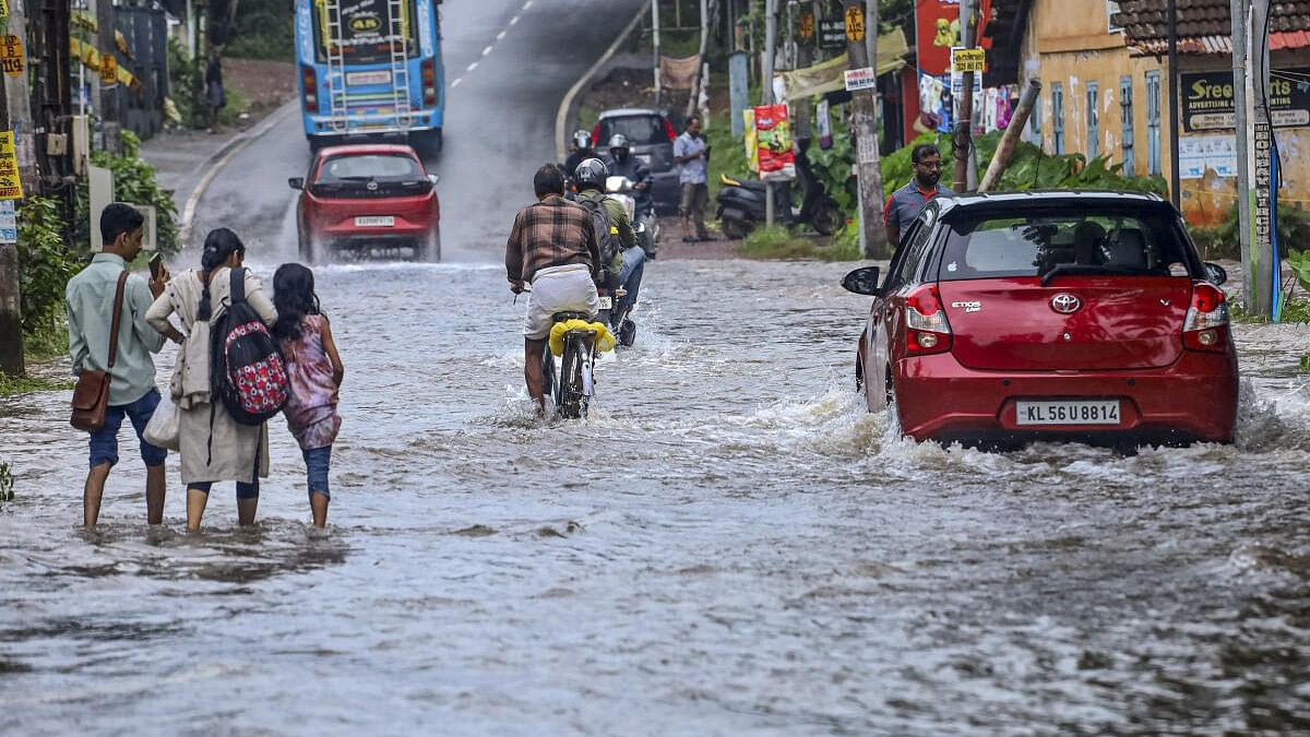 <div class="paragraphs"><p>Commuters make their way through a flooded road following rains, in Kozhikode.</p></div>