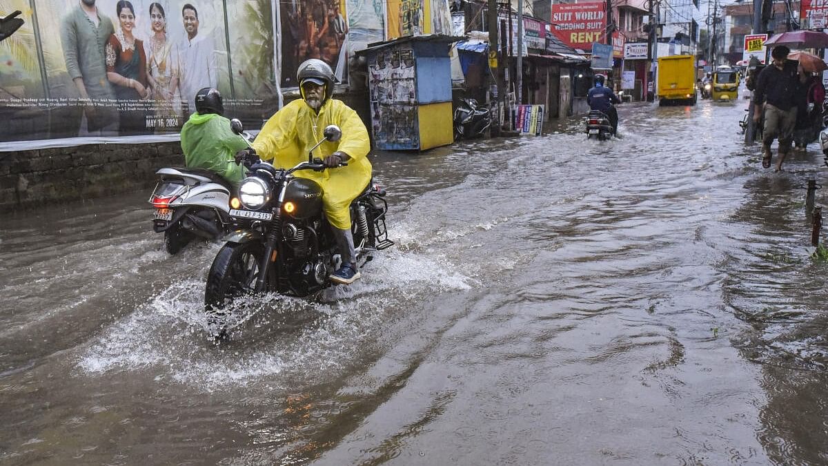 <div class="paragraphs"><p>Commuters wade through a flooded road amid rains, in Kochi.</p></div>