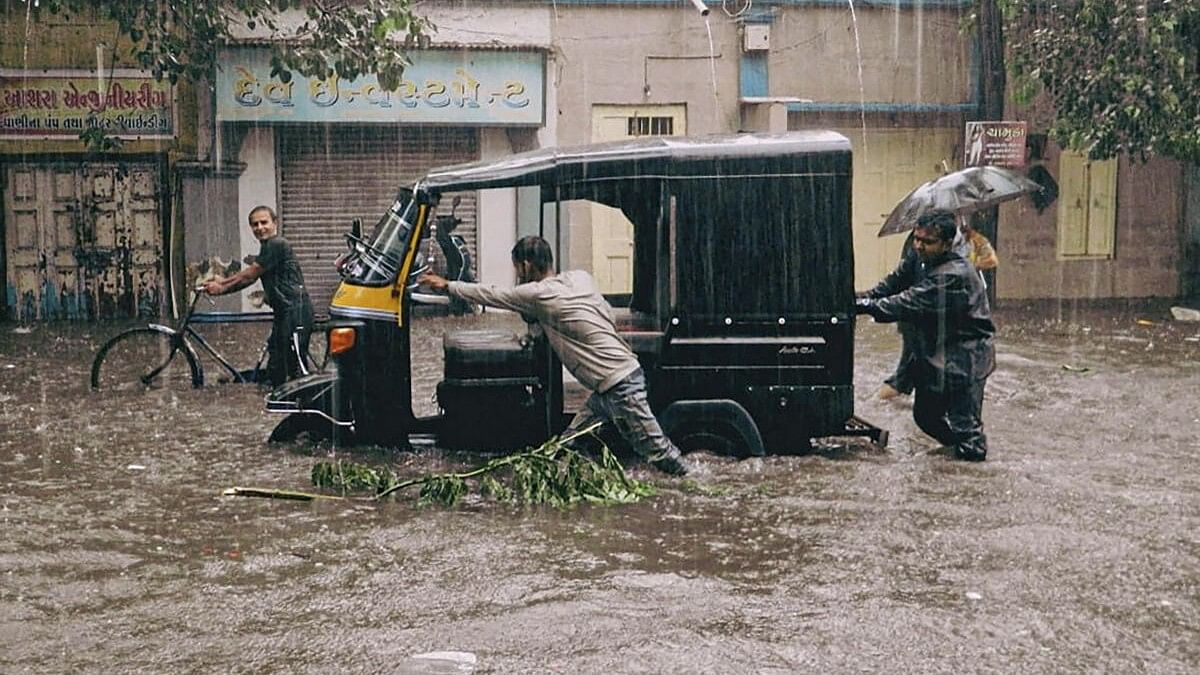 <div class="paragraphs"><p>Passengers and a driver push an auto rickshaw through a flooded road after heavy rains in Gujarat.&nbsp;</p></div>