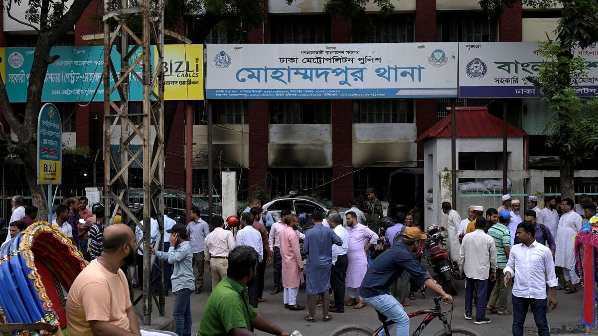 <div class="paragraphs"><p>People stand in front of a police station that was partially damaged by a mob during recent clashes in Dhaka.</p></div>