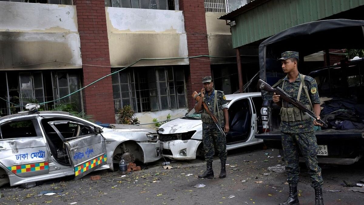 <div class="paragraphs"><p>Security force personnel stand guard next to damaged vehicles outside a police station, in Dhaka</p></div>