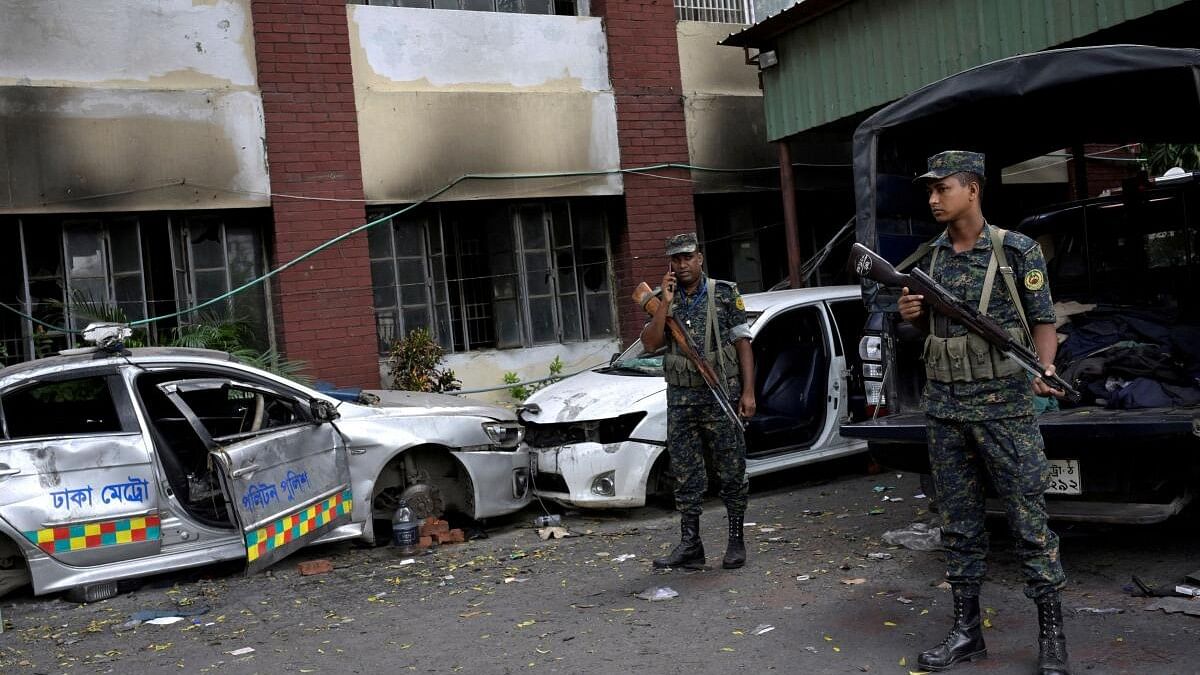 <div class="paragraphs"><p>Security force personnel stand guard next to damaged vehicles outside a police station, days after the resignation of former Bangladeshi Prime Minister Sheikh Hasina.</p></div>