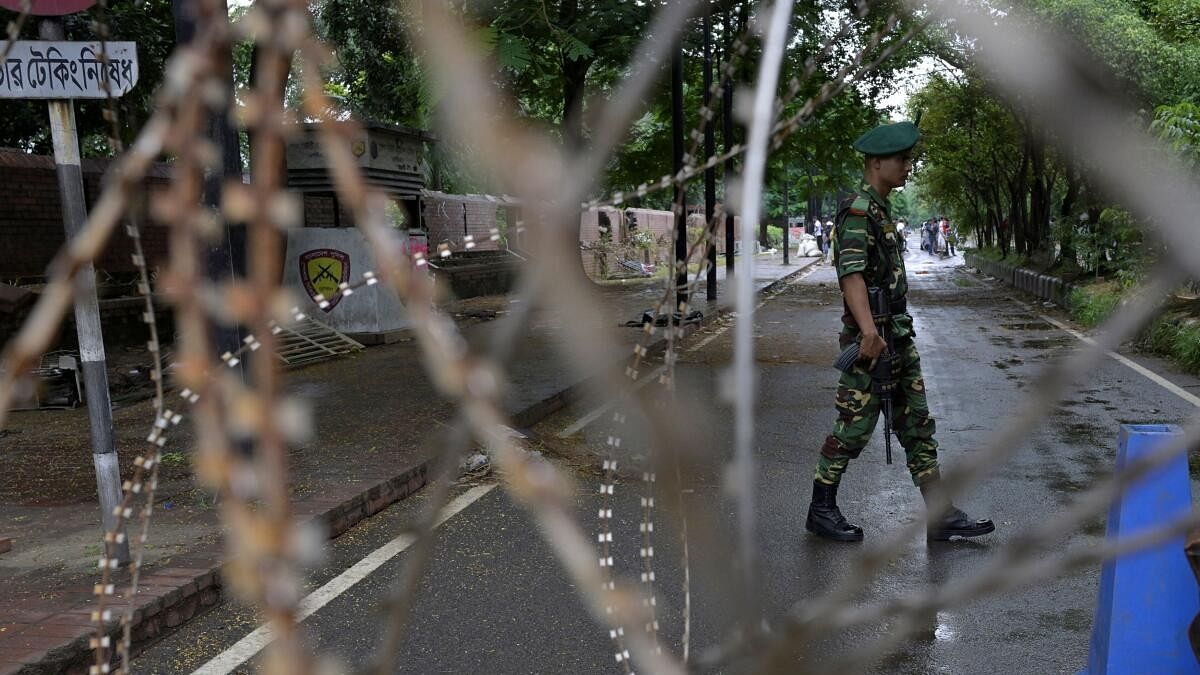 <div class="paragraphs"><p>A security force personnel walks behind concertina wire placed across a road next to the residence of Sheikh Hasina, in Dhaka</p></div>