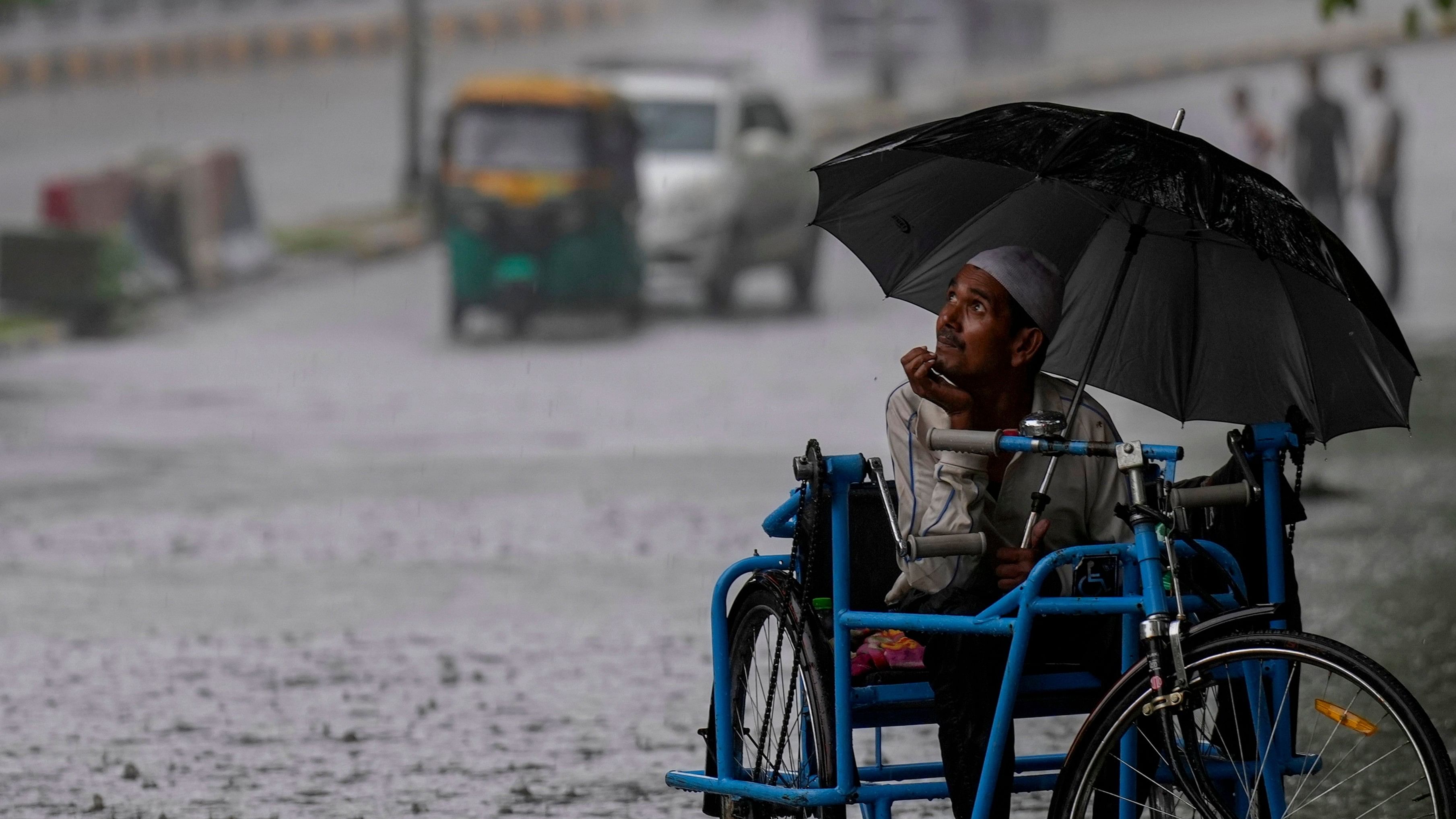 <div class="paragraphs"><p>A physically challenged man looks towards the sky as he travels through a waterlogged road amid monsoon rain, in New Delhi.</p></div>