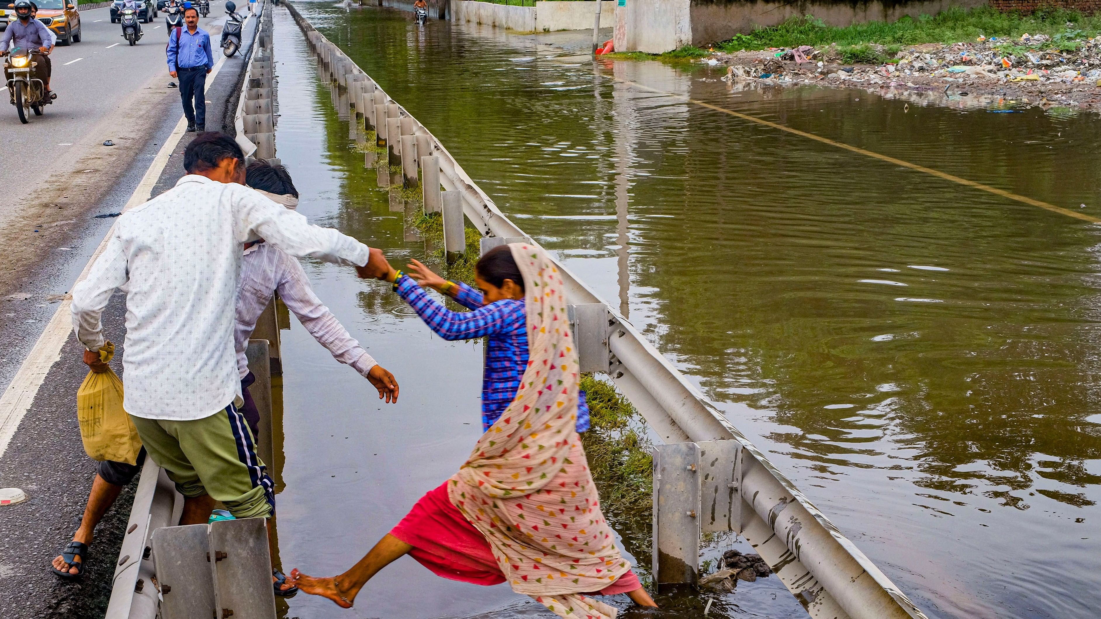 <div class="paragraphs"><p><ins>A</ins> woman tries to cross a deep drain next to the waterlogged road.&nbsp;</p></div>