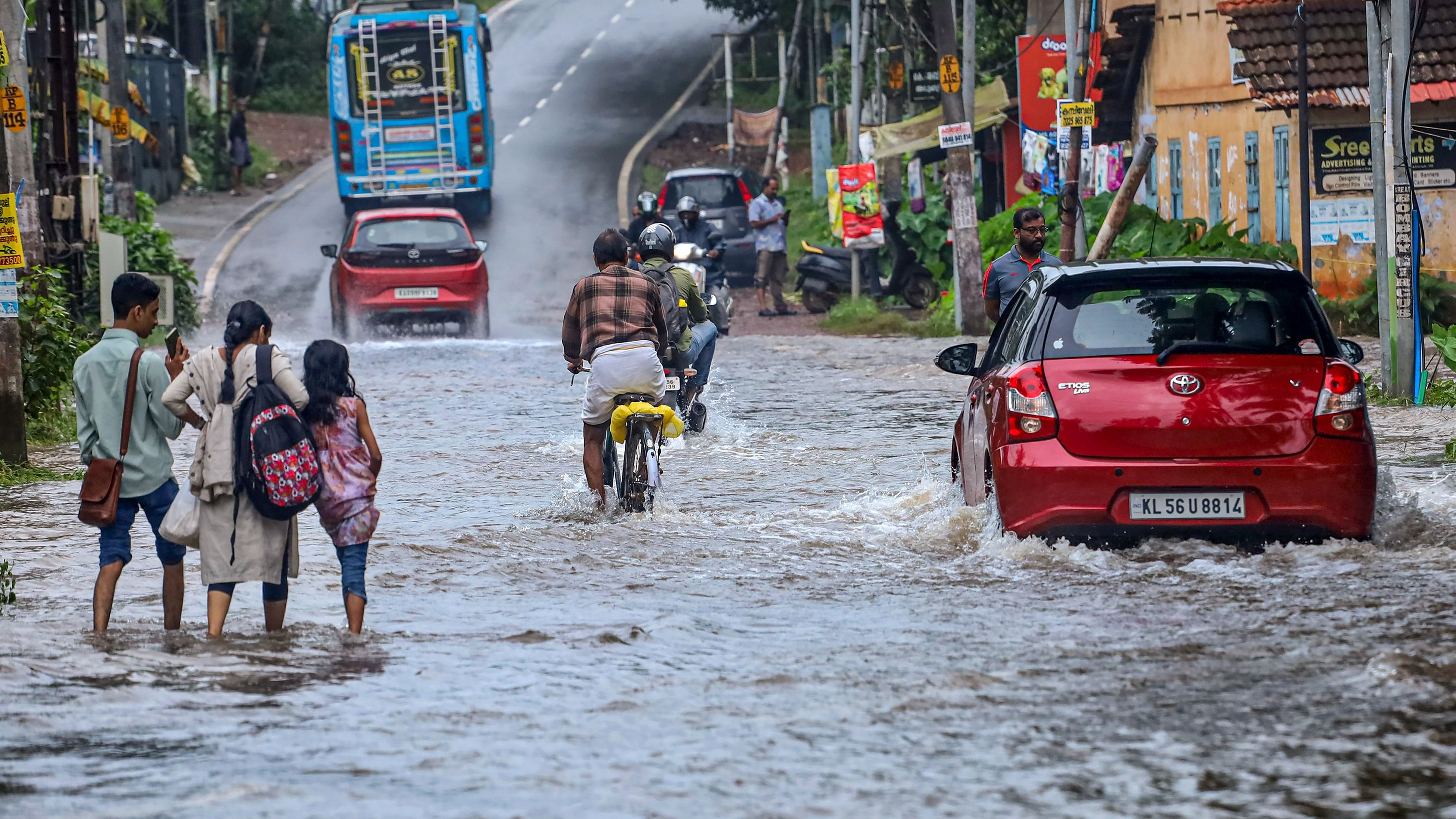 <div class="paragraphs"><p> Commuters make their way through a flooded road following rains in Kozhikode.</p></div>