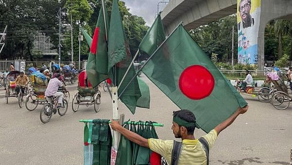 <div class="paragraphs"><p>A flag-seller stands on the periphery of a memorial site, overlooking the tainted mural of first president of Sheikh Mujibur Rahman on the pier of a metro line, days after the anti-government protests that ousted the then Bangladesh prime minister Sheikh Hasina, near Dhaka University.</p></div>