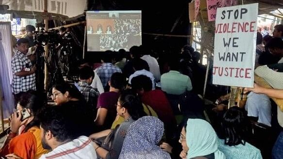 <div class="paragraphs"><p>Resident doctors of RG Kar Medical College and Hospital watch live streaming of the Supreme Court hearing in the alleged rape and murder of a trainee woman doctor inside the hospital during their protest, in Kolkata, Thursday, Aug. 22, 2024.</p></div>