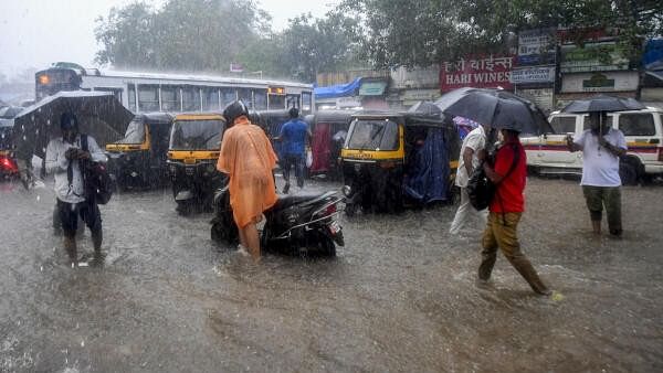 <div class="paragraphs"><p>Commuters pass through a waterlogged road after heavy rainfall outside the Kurla station, in Mumbai.</p></div>