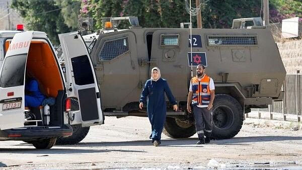 <div class="paragraphs"><p>An ambulance crew member and a woman walk near an ambulance, as an Israeli military vehicle takes part in a raid, in Jenin, in the Israeli-occupied West Bank.</p></div>