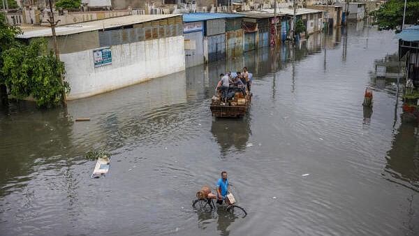 <div class="paragraphs"><p>People cross a flooded street after heavy rains in Gujarat.</p></div>