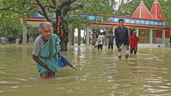 <div class="paragraphs"><p>An elderly women and other people walk through a flooded area after the Kankalitala Temple got partially submerged due to rains, in Birbhum district.</p></div>