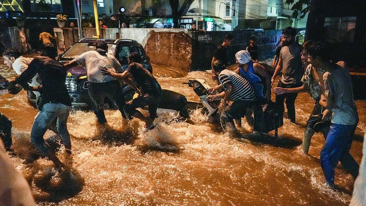 <div class="paragraphs"><p> People try to pull a two-wheeler from being swept away by rainwater in Delhi</p></div>