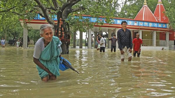 <div class="paragraphs"><p>An elderly women and other people walk through a flooded area after the Kankalitala Temple got partially submerged due to rains, in Birbhum district.&nbsp;</p></div>