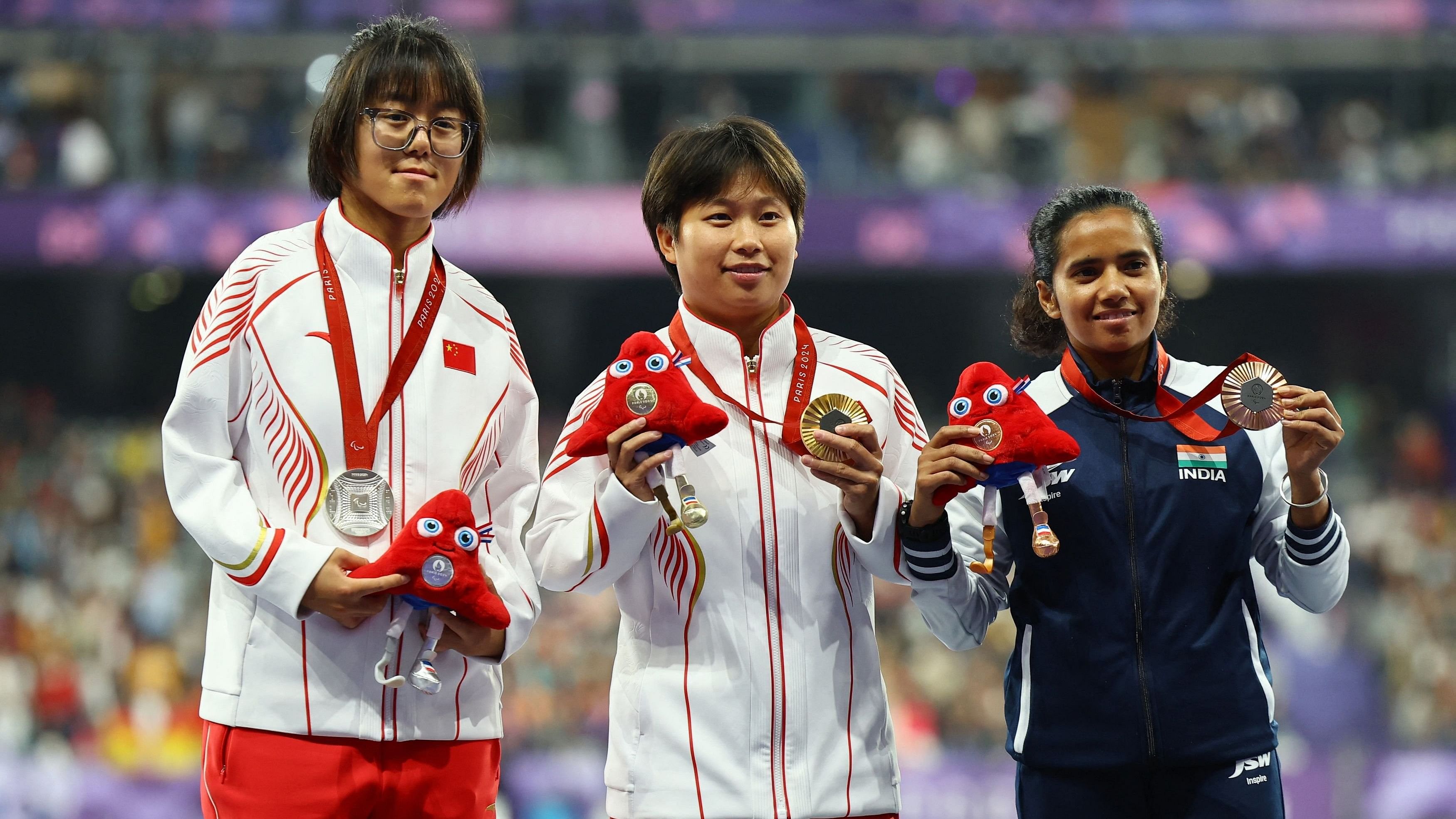 <div class="paragraphs"><p>Gold medallist Xia Zhou of China celebrates on the podium during the victory ceremony alongside Silver medallist Qianqian Guo of China and Bronze medallist Preethi Pal of India.</p></div>