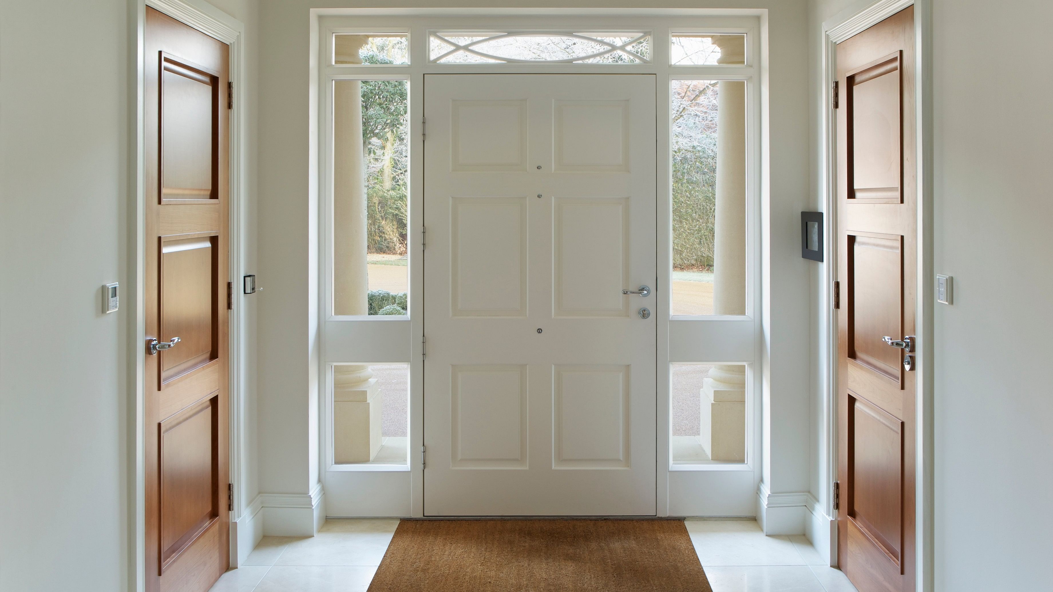 <div class="paragraphs"><p>Afront door entrance to a grand house. The wood panelled front door and frame are painted white whilst either side, also in white frames are two wooden doors for two separate cloakrooms. </p></div>