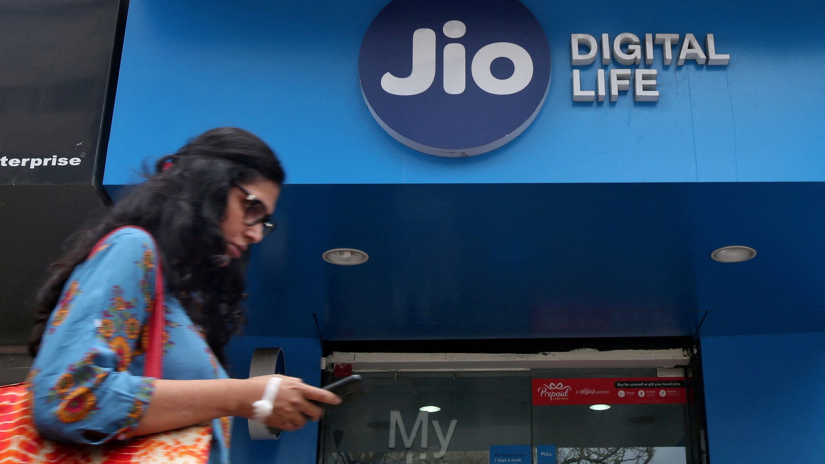 <div class="paragraphs"><p>FILE PHOTO: A woman checks her mobile phone as she walks past a mobile store of Reliance Industries' Jio telecoms unit, in Mumbai.</p></div>