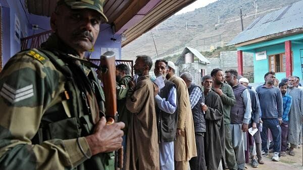 <div class="paragraphs"><p>An Indian Border Security Force personnel stands guard as people wait a line to cast their vote outside a polling station during the third and final phase of the assembly election, in north Kashmir's Bandipora district October 1.</p></div>