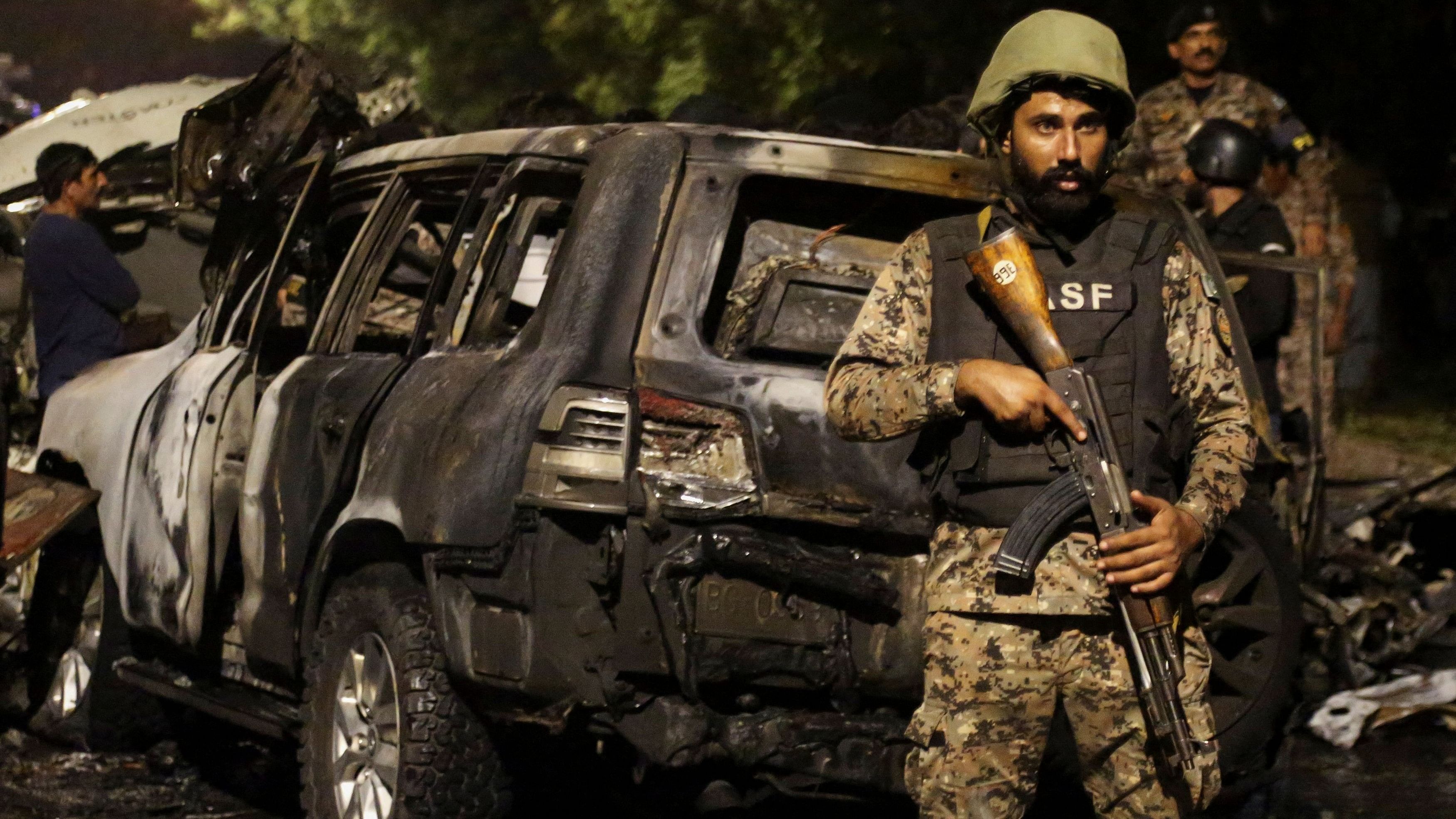 <div class="paragraphs"><p>Airport Security Force stand guards near the wreckage of vehicles after an explosion near Jinnah International Airport in Karachi</p></div>