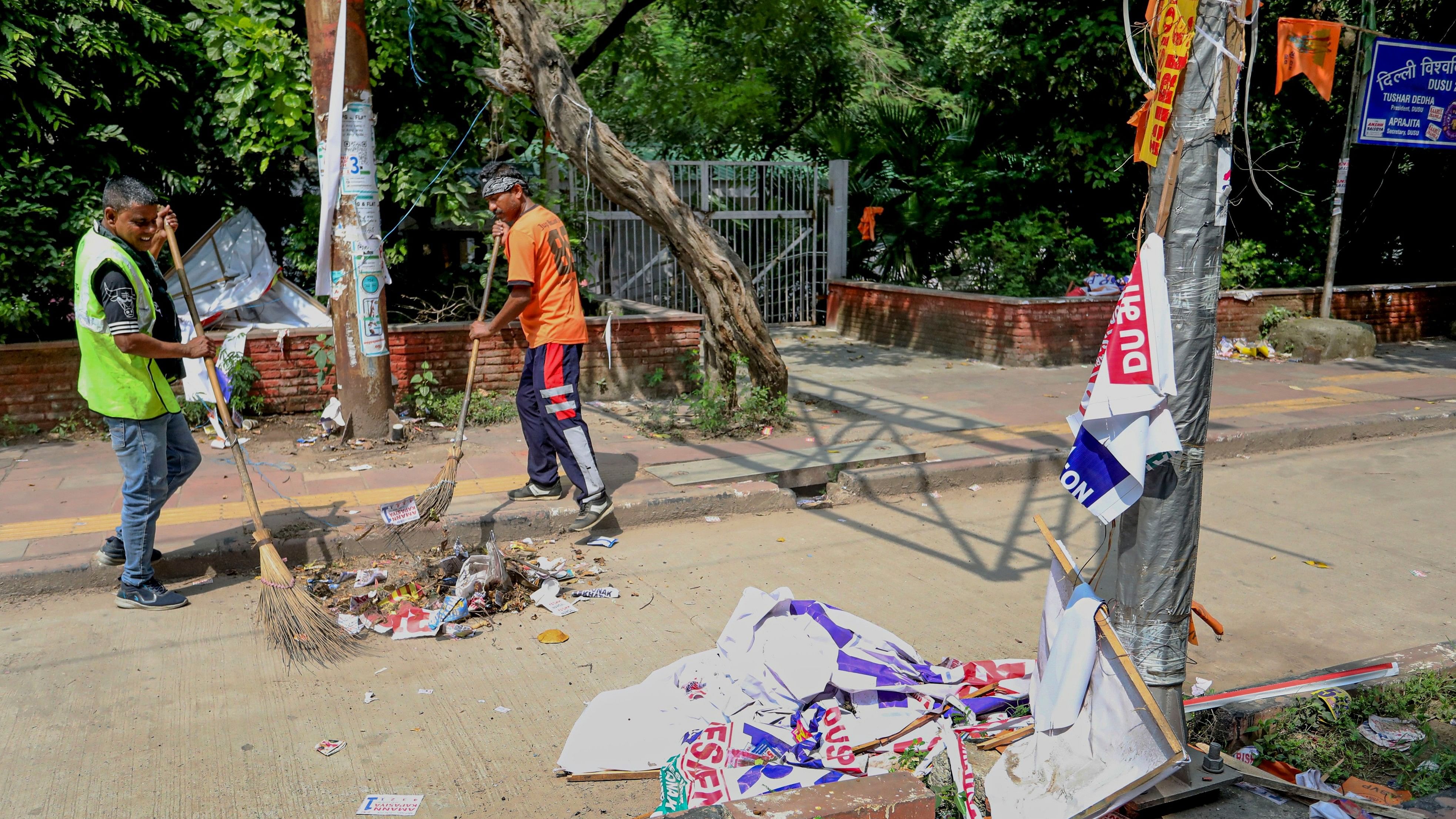 <div class="paragraphs"><p>Workers clear banners and posters from an area after the Delhi University Students' Union (DUSU) polls at North Campus in New Delhi.</p></div>