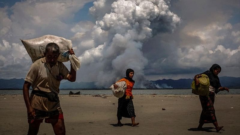 <div class="paragraphs"><p>Smoke is seen on the Myanmar border as Rohingya refugees walk on the shore after crossing the Bangladesh-Myanmar border by boat through the Bay of Bengal, in Shah Porir Dwip, Bangladesh in this file photo.</p></div>